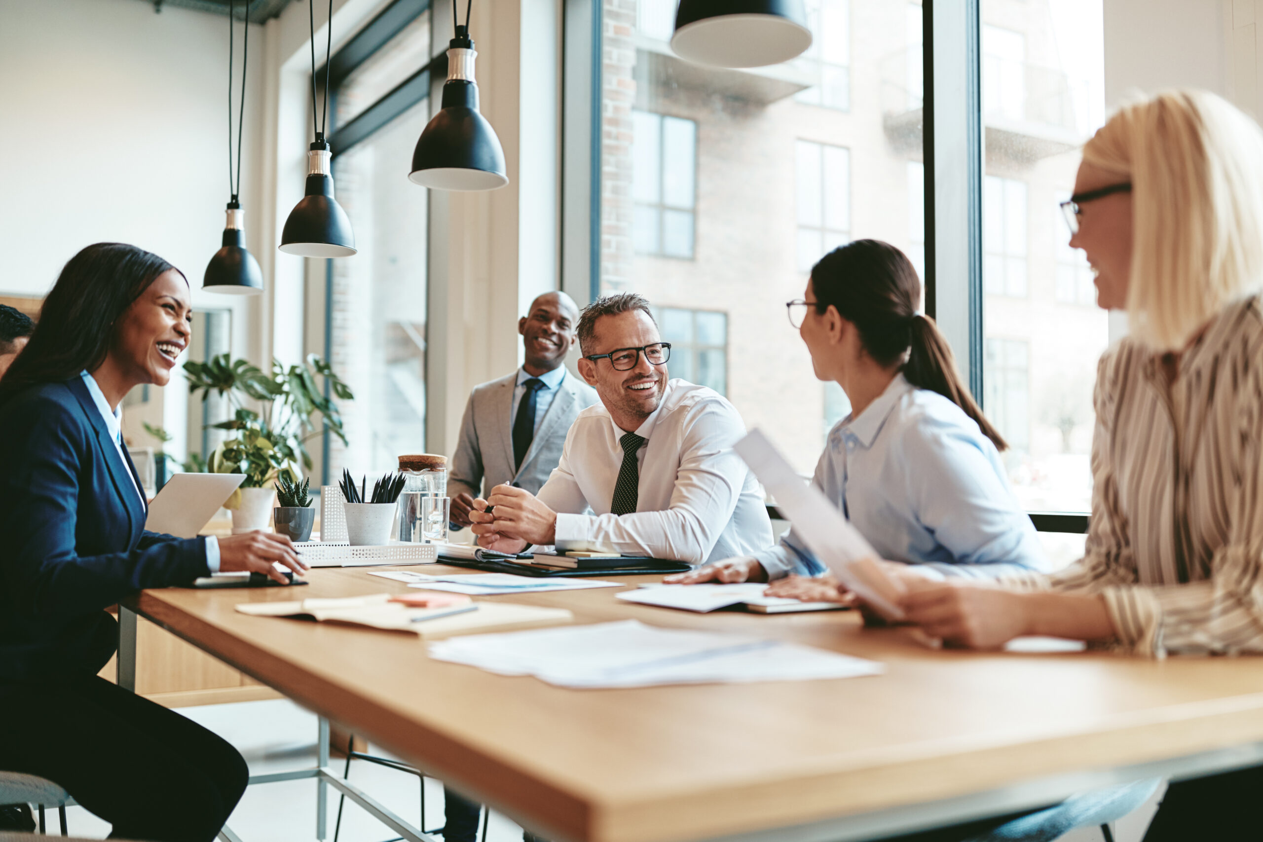 Diverse group of business people laughing while discussing paperwork together during a meeting around a table in a modern office.