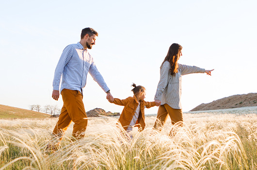 A young family of three walking through a field of tall, light-colored grass