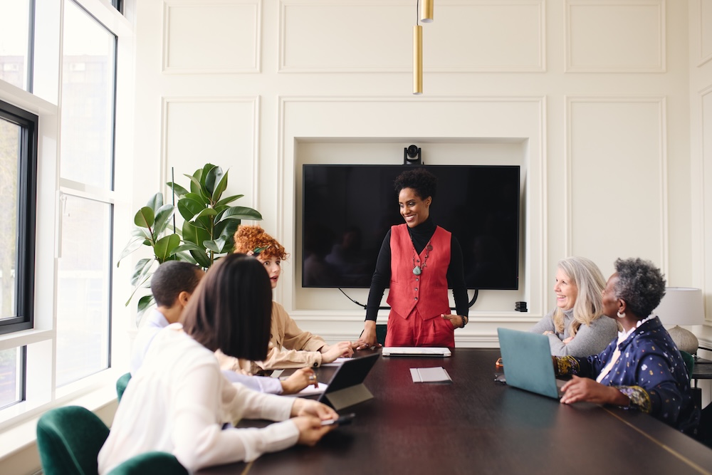 Portrait of cheerful mature black businesswoman discussing with female colleagues in meeting room