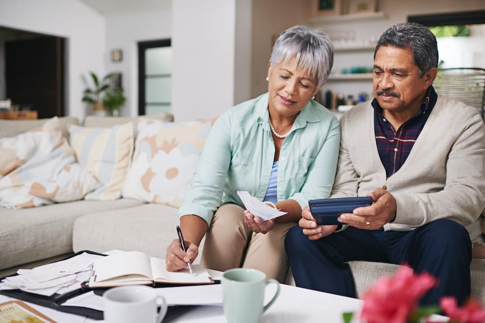 An older couple sat on a sofa indoors are organising their finances