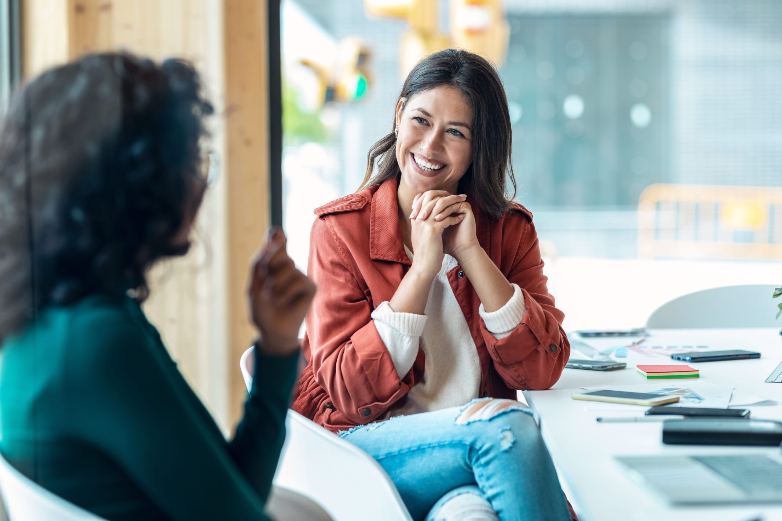 Two women are talking at a desk, one is smiling