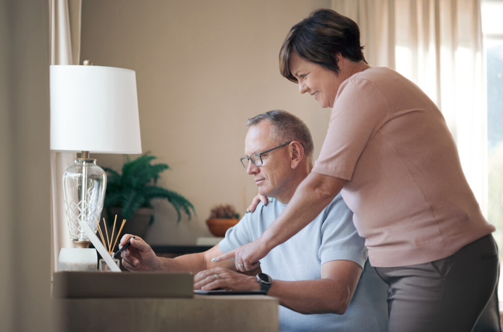 A man and woman looking at a desktop screen in a softly-lit home workspace.